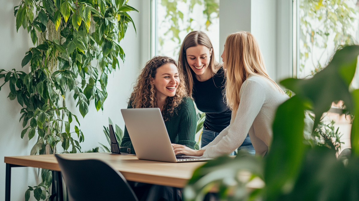 Three colleagues laughing together at a laptop